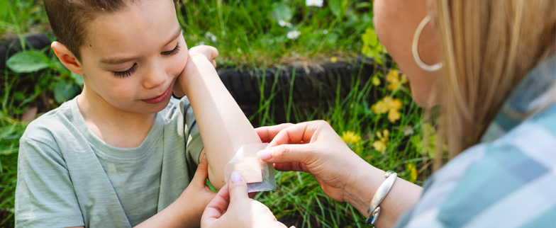 A parent is putting a band-aid on their child's elbow to cover a scrape.