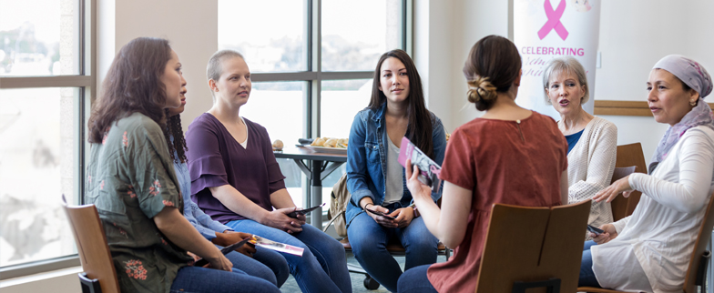 Group of adults sitting on chairs set in a circle talking about breast cancer awareness.