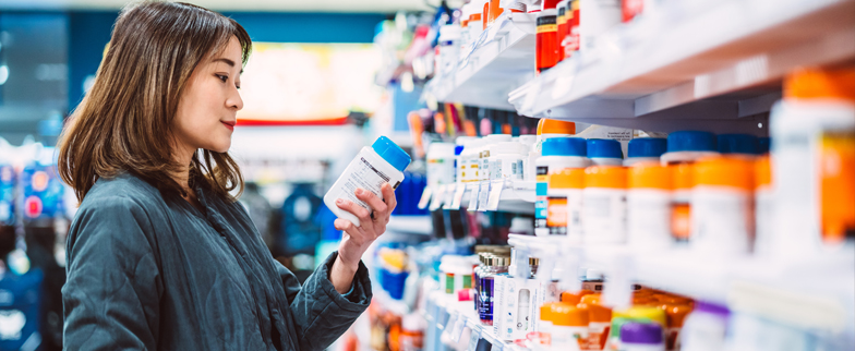 Adult reading a medication bottle in the pharmacy section of a store.