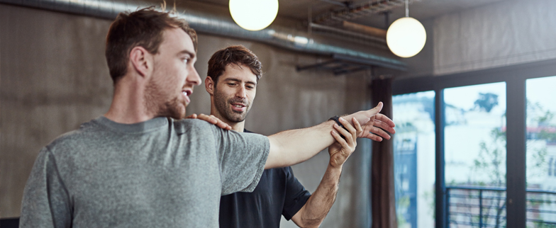 A workout trainer helping an adult stretch their arm at a gym